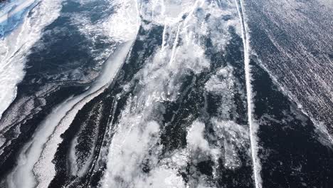 drone footage of a frozen lake, highlighting intricate ice formations and cracks from above, showcasing nature's abstract designs