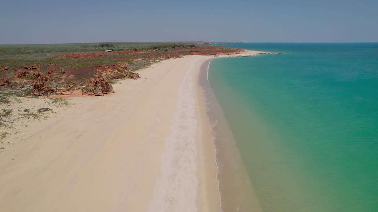 Lot dronem wzdłuż Barn Hill Beach w Australii Zachodniej, uchwycenie turkusowej wody, białego piasku, czerwonych klifów i formacji skalnej przypominającej zaginione miasto w tętniącej życiem nadmorskiej scenerii