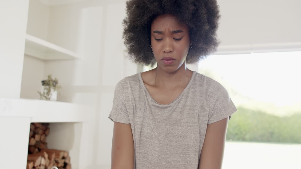 African American woman holding purple weights, lifting at home, pausing, glancing, resuming workout