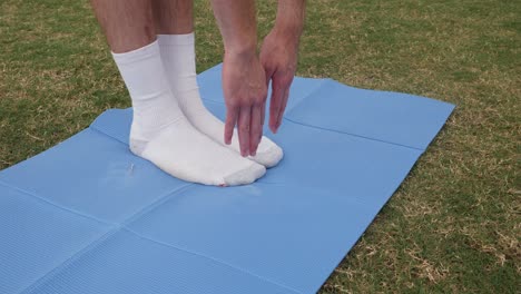 man touches his toes on a blue yoga mat in the grass