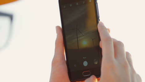 close-up view of smartphone screen with photos of the huge windmills tourbines at the sunset