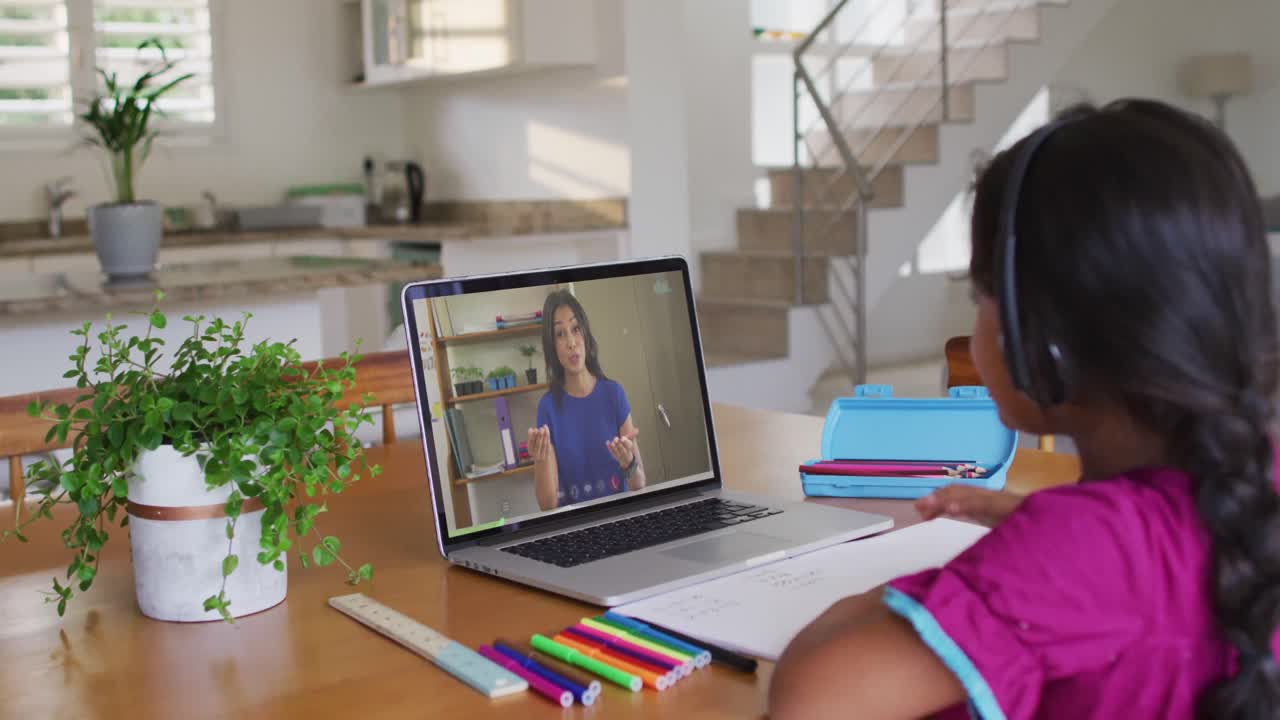 chica afroamericana haciendo la tarea mientras tiene una videollamada con una maestra en una computadora portátil en casa