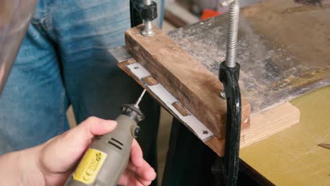 woman polishings a small sheet of metal of a door lock with a small die grinder and with protection gear on her face as a man aproaches