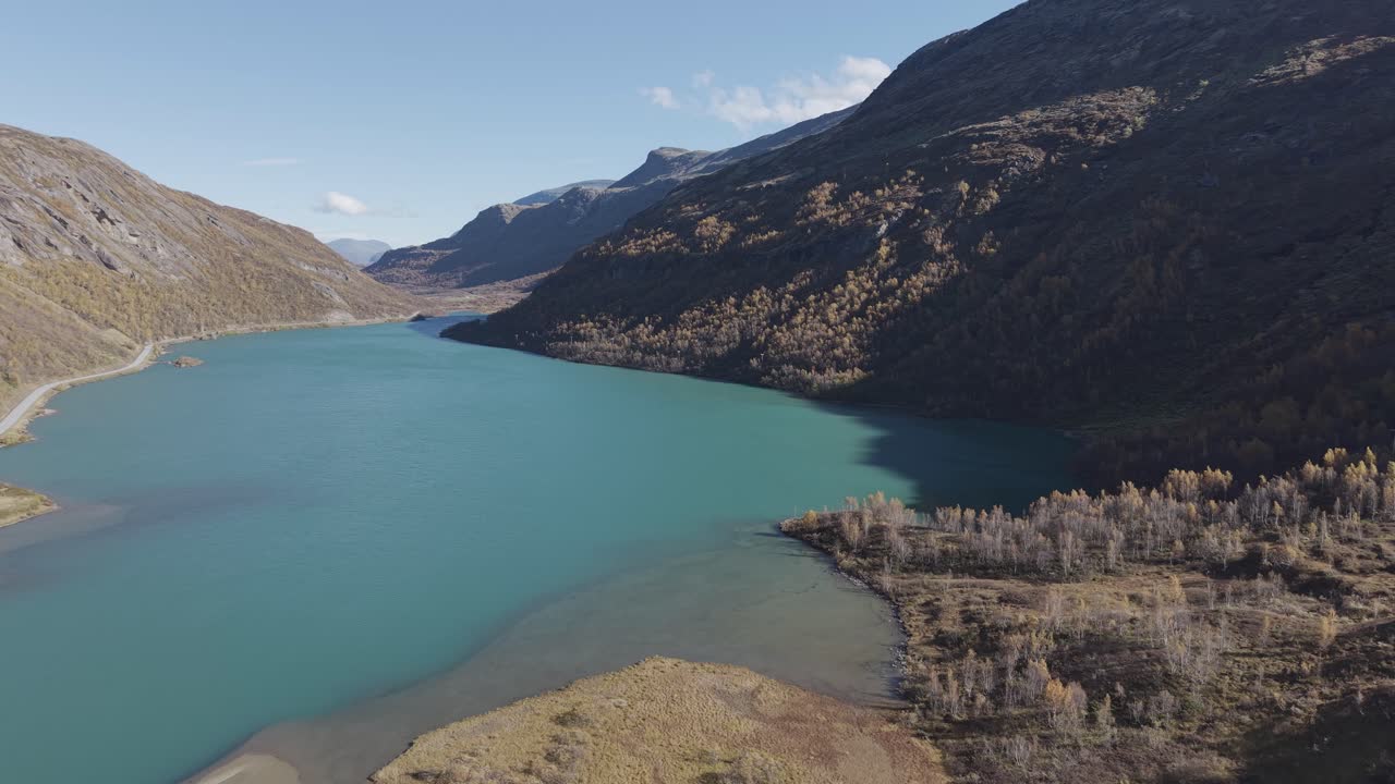 A drone-filmed view of a glacial lake with striking turquoise-green waters in Jotunheimen, surrounded by autumn mountains