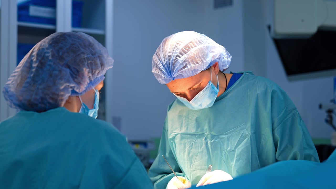Operazione chirurgica eseguita dalla chirurga e dall'infermiera strumentista. Il medico usa strumenti metallici durante l'intervento.