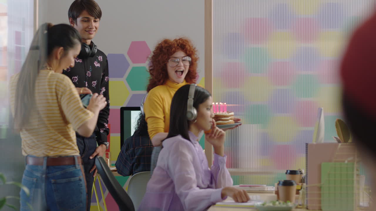 젊은 사업가 들 이 생일 파티 를 축하 하고 있다. 행복 한 혼혈 인종 의 여성 들 이  ⁇ 불 을 불어서 놀라움을 즐기고 있다. 친구 들 은 다채로운 사무실 축제 에서 함께 환호 하고 있다.