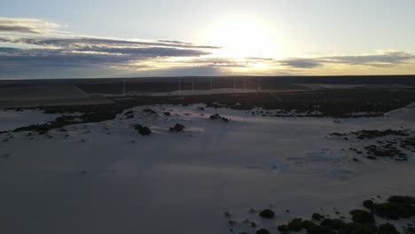 avión no tripulado sobre dunas de arena cerca de molinos de viento durante el amanecer