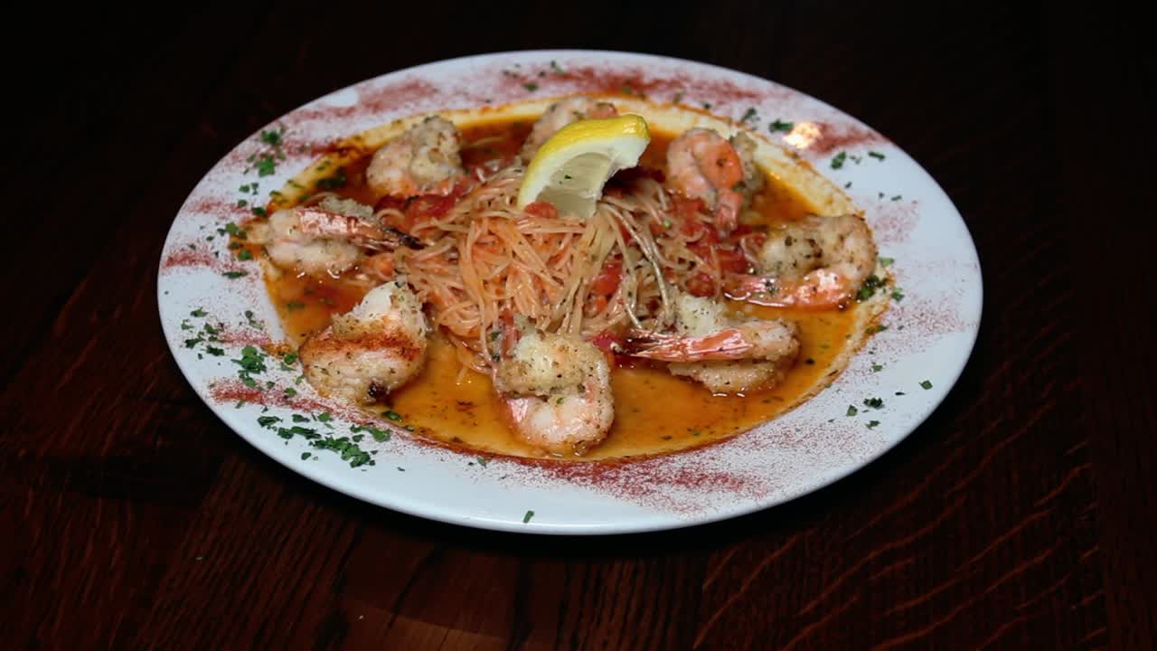 A close-up shot of a flavorful seafood pasta on a white plate, featuring shrimp over spaghetti in a spicy tomato sauce, garnished with a lemon wedge and fresh herbs.