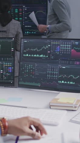 financial analyst spins pencil in hand, works in bank office. real-time stocks, exchange market charts and tv news displayed on computer monitors. analytics and cryptocurrency trading. vertical shot