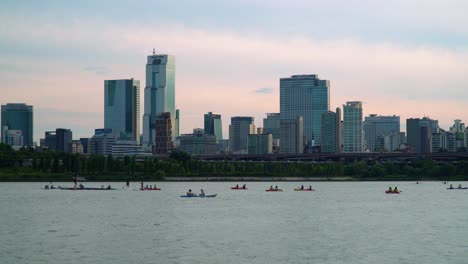 Gruppe-Von-Menschen,-Die-Auf-Dem-Han-fluss-Mit-Seoul-stadtskylinen-Auf-Buntem-Sonnenunterganghimmelhintergrund-Kajak--Oder-Kanufahren