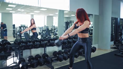 athletic young woman doing various strength exercises with weights. beautiful woman with muscular body swinging heavy kettlebell in her hands near the mirror in fitness center.