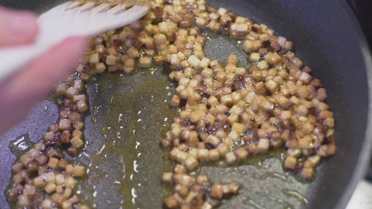 rebanadas de tofu ahumado frito chisporroteando en una sartén con aceite