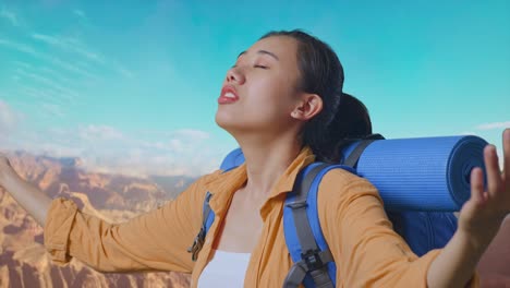close up side view of asian female hiker with mountaineering backpack spreading arms enjoy looking the view around while traveling at the top of mountain