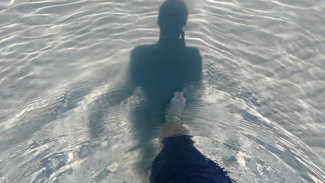 person walks in clear, rippling water over sandy bottom, creating a serene scene