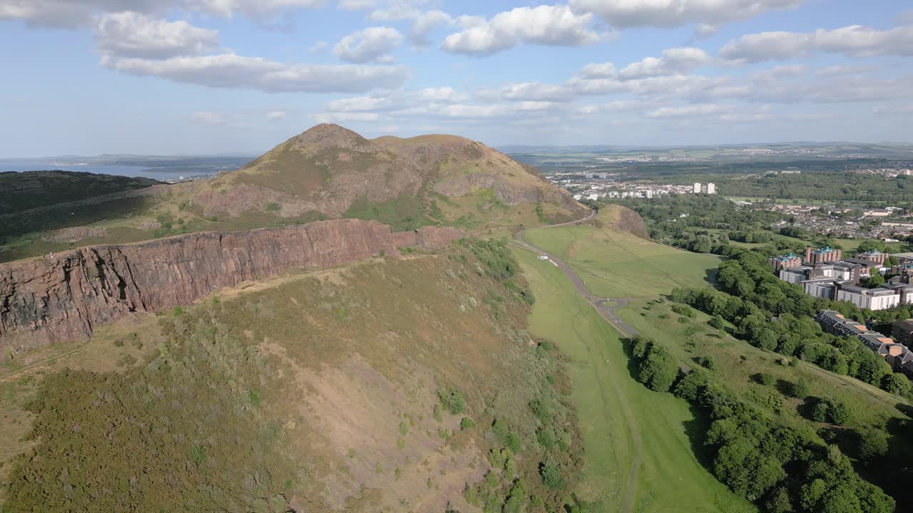 Sunny aerial push in of Edinburgh's Arthur Seat surroundings on a group of green hills, Edinburgh, Scotland, UK