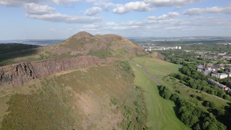 sunny aerial push in of edinburgh's arthur seat surroundings on a group of green hills, edinburgh, scotland, uk
