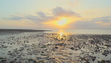 Moving-over-wet-shoreline-towards-calm-sea-and-breakwater-during-sunset-in-slow-motion-at-Fleetwood,-Lancashire,-UK