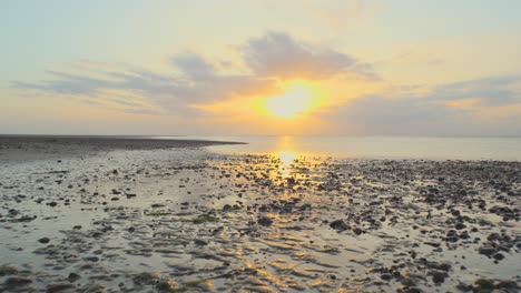 moviéndose sobre la costa húmeda hacia el mar tranquilo y el rompeolas durante la puesta de sol en cámara lenta en fleetwood, lancashire, reino unido
