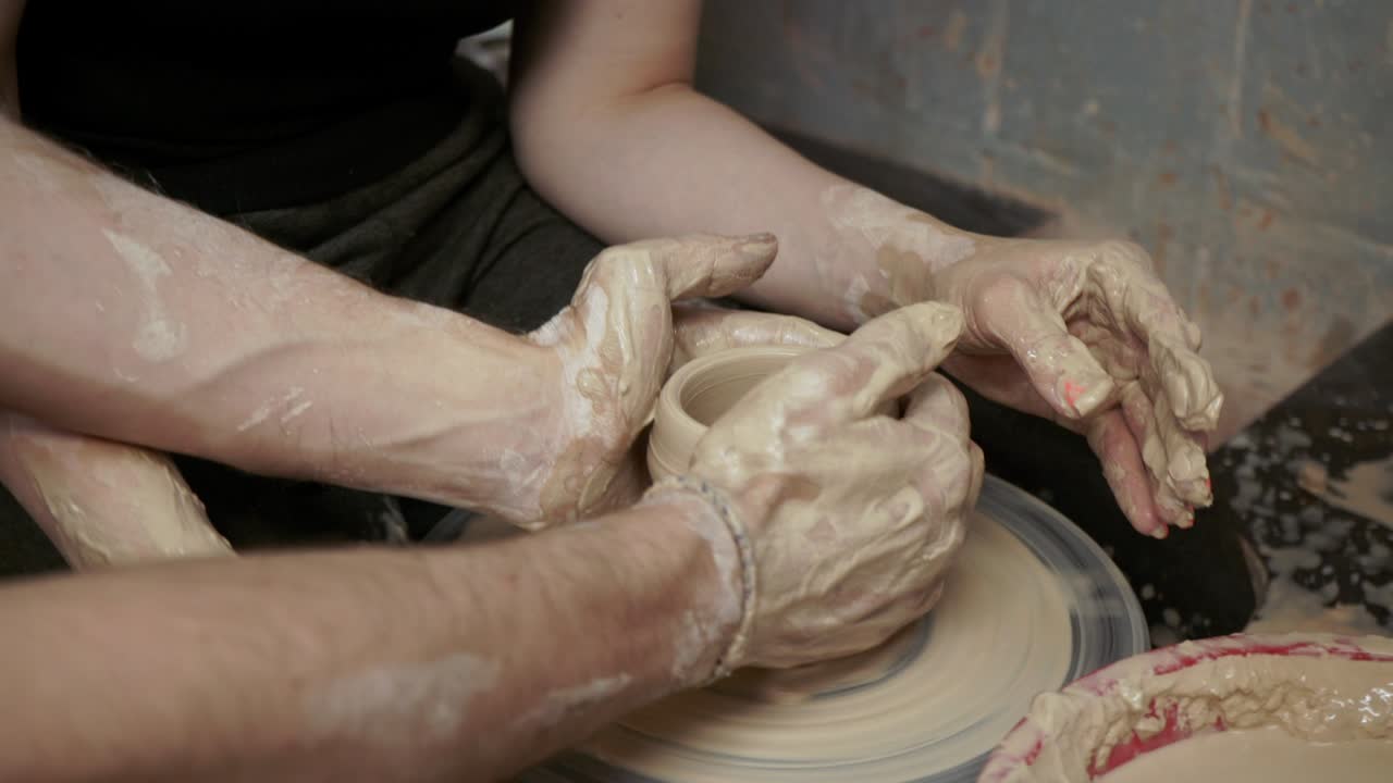 un alfarero enseña a una mujer a hacer platos de arcilla. un hombre toma las manos de una mujer