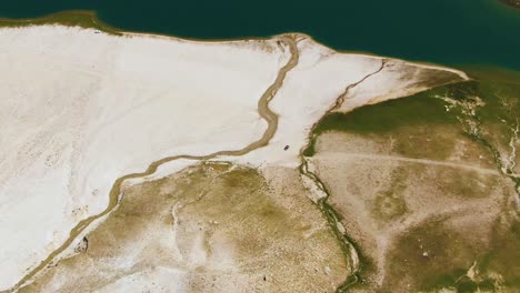 people horseback riding on a white sand of arashan lakeshore on a sunny day in summer in uzbekistan