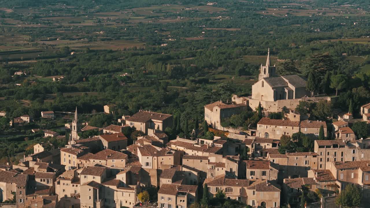 Aerial flyover of Bonnieux, Provence, France, showcasing the historic village’s scenic rooftops and countryside landscape glowing orange from sunlight