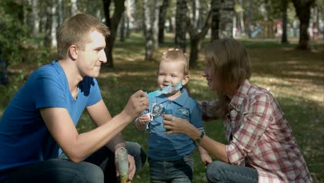 boy is playing together with his parents. they are playing with soap-bubbles