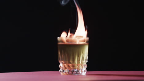 a flaming cocktail stands on a bar counter, creating a dramatic effect