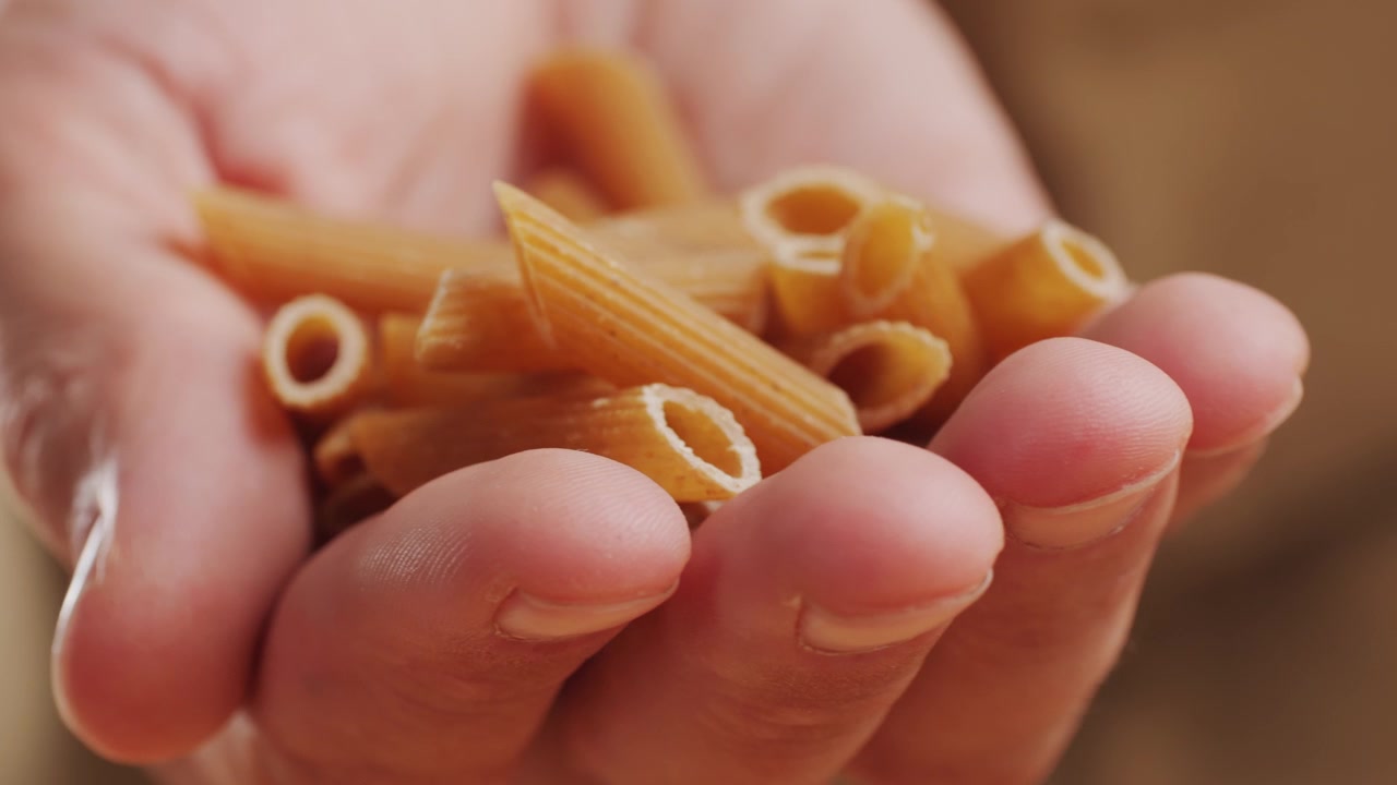 Pasta integrale biologica, maccheroni di semola di grano duro, penne rigate crude in una ciotola di legno. Filmato 4k di alta qualità