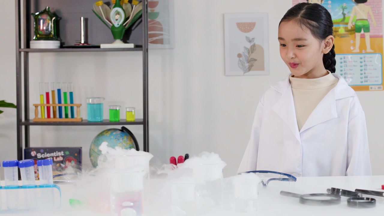 白い白衣を着た若いアジア人の少女が、科学の実験中にドライアイスの蒸気を観察している