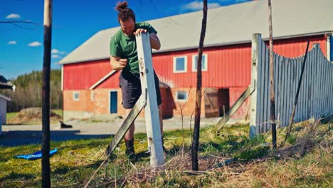 caucasian man fixing a wooden fence in a countryside village. static shot