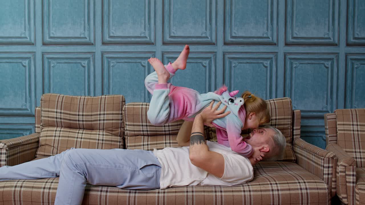 niña volando como un avión, jugando a un juego riendo con un padre joven, relajándose en el sofá en casa
