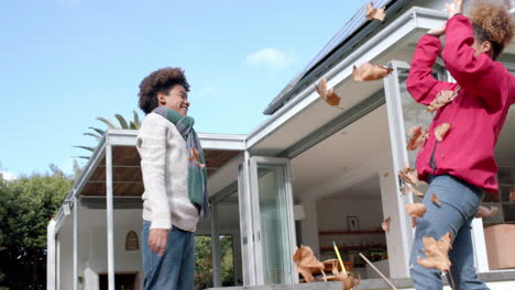 happy african american mother and son in scarf playing with leaves in sunny garden, in slow motion