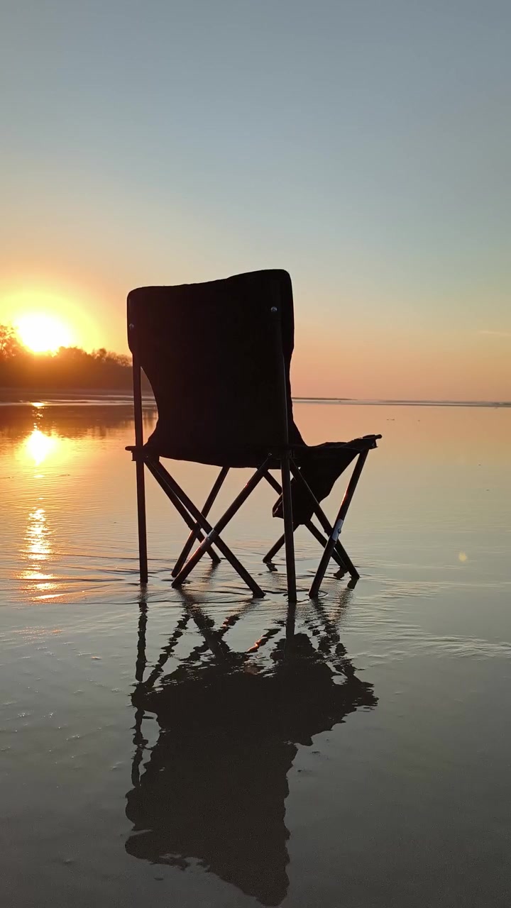 Jeune homme près d'une chaise pliante sur la plage au coucher du soleil