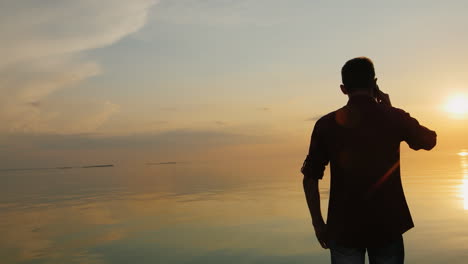 Teen-Boy-Telefoniert-Am-Meer-Bei-Sonnenuntergang-Rückansicht