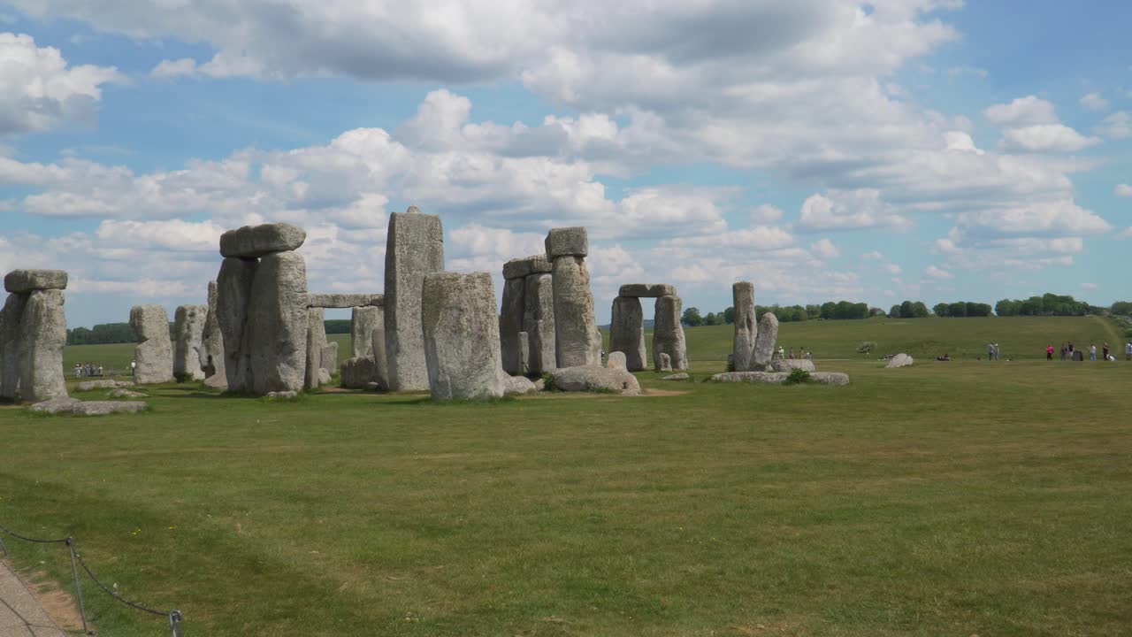 Close up view to the Stonehenge a prehistoric megalithic structure on Salisbury plain in Wiltshire England. Steady camera with a group of tourists walking on the background, blue sky with some clouds.