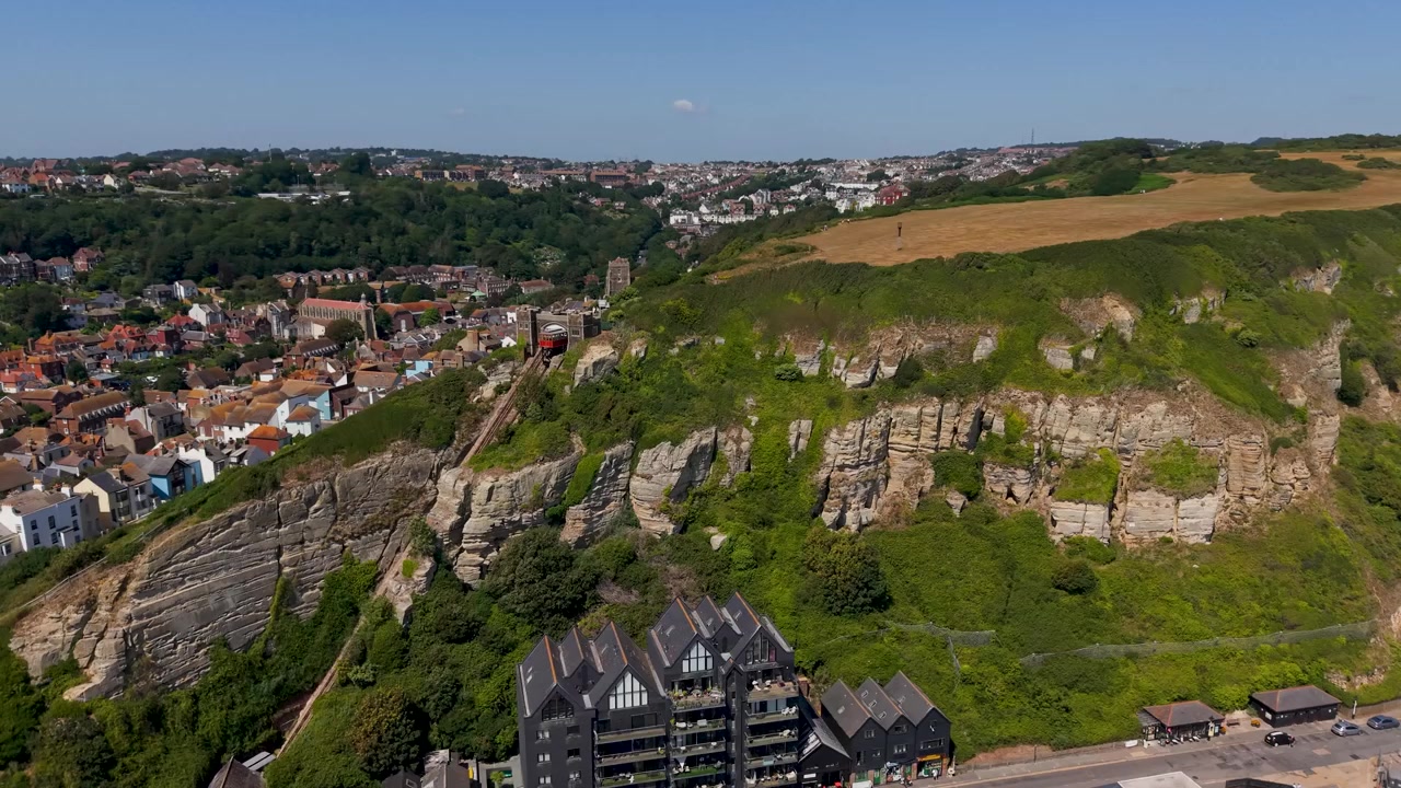 Funicular de East Hill en Hastings visto desde la órbita de un dron, vagones estáticos en un ferrocarril de acantilado empinado sobre el casco antiguo y la costa, revelando un gradiente y dramáticos acantilados de tiza con luz de verano