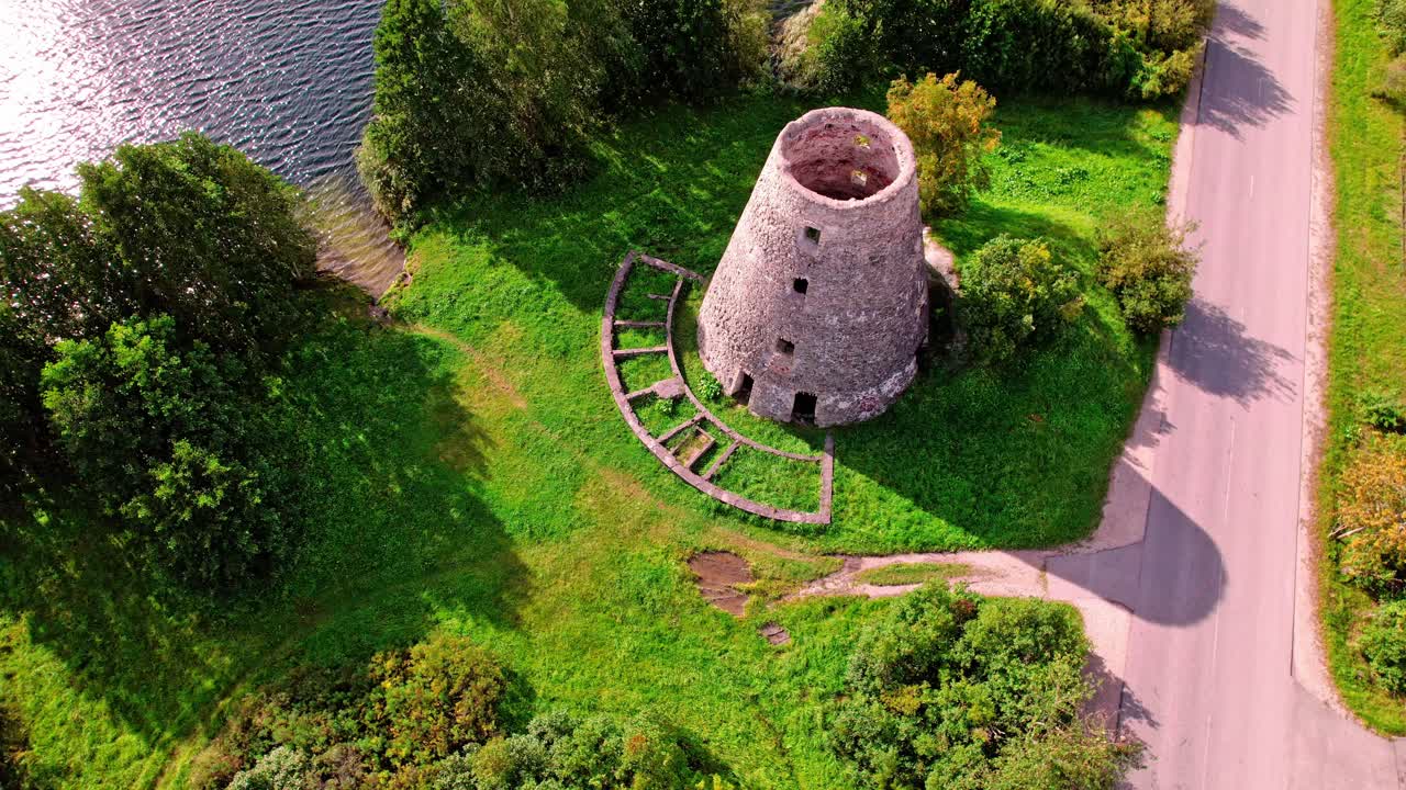 Historic tower sits among lush greenery near the river in Latvia