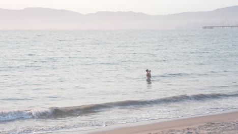 young-mother-holding-her-baby-in-the-waves,-slowmotion