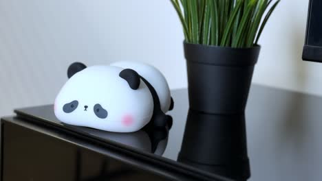 close-up of a hand pressing a glowing panda-shaped night light on a black glass table. captures cozy ambiance, adorable design, and home decor aesthetics in crisp 4k.