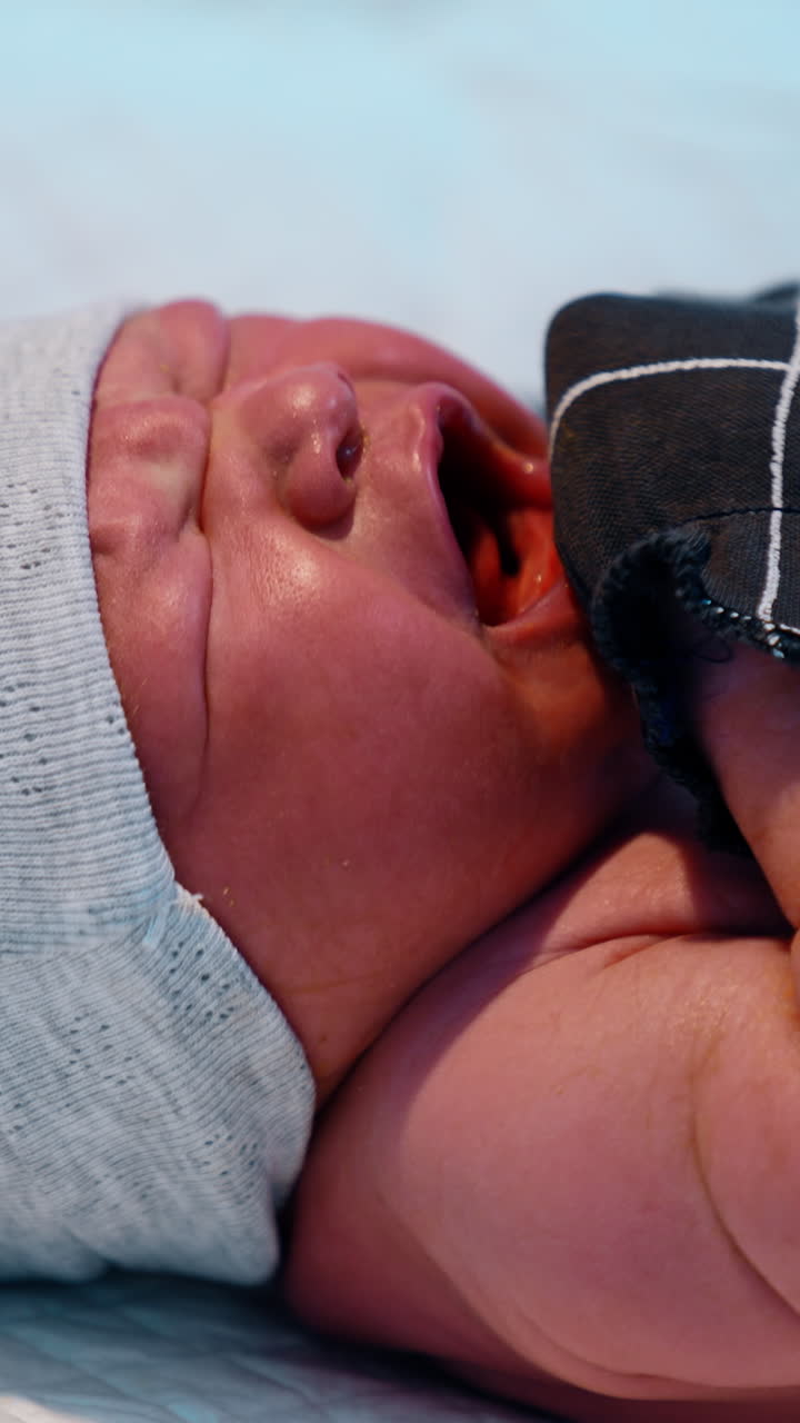 Newborn baby in cap and mittens is screaming bitterly. Medic is putting the diaper on the child. Close up. Vertical video
