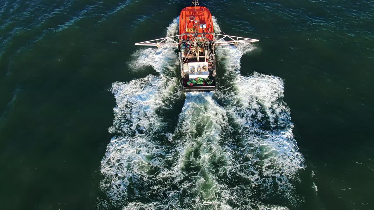 Overhead of Prawn trawler leaving to fish from harbor at sunset  .Drone