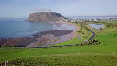 amazing aerial flight over green field away from rock in tasmania, australia