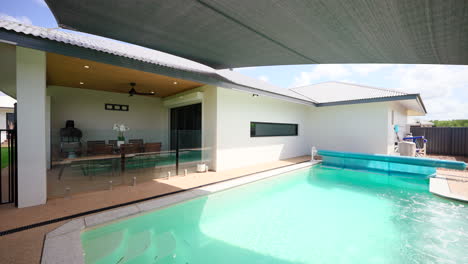 large display home pool area with white wall black roof and shade cloth half covering backyard