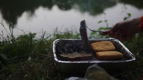 Video-footage-shows-person-using-an-iron-grill-to-cook-bread-and-meat-next-to-a-body-of-water