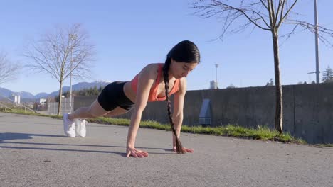 young woman doing pushups on pavement, handheld circle pan left