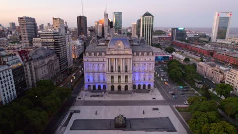 dolly in aerial view of the front of the kirchner cultural center illuminated with blue lights, city at night during the blue hour, buenos aires, argentina