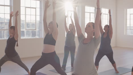 yoga class of young pregnant women practicing warrior pose enjoying healthy lifestyle group fitness workout in exercise studio at sunrise