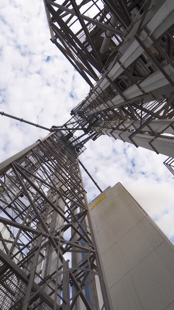 Metal towers on industrial plant. Steel construction on a modern agricultural factory with grain elevators on sky background. View from below. Vertical video