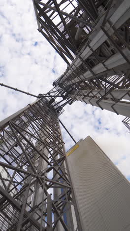 metal towers on industrial plant. steel construction on a modern agricultural factory with grain elevators on sky background. view from below. vertical video