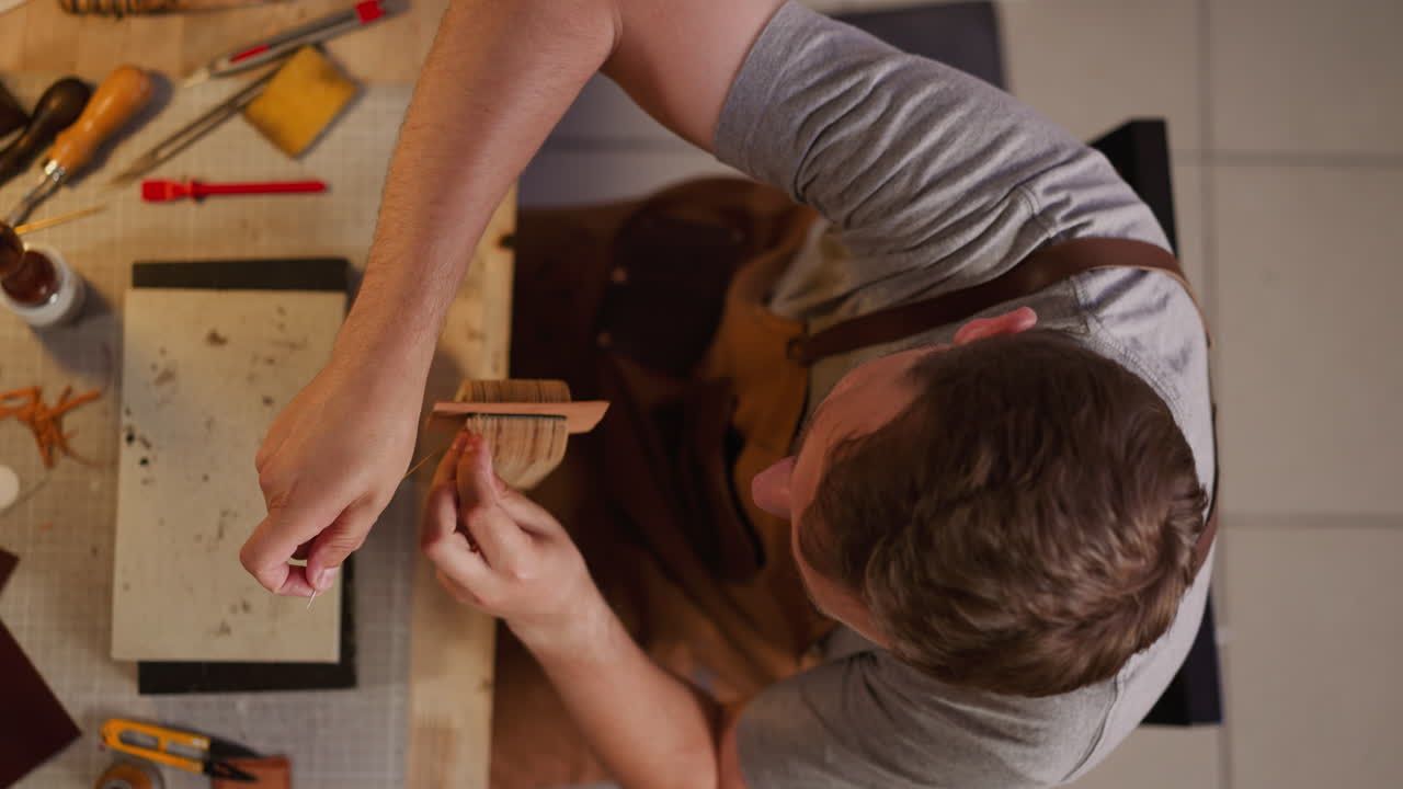 Tailor sews leather with waxed thread at table in workshop